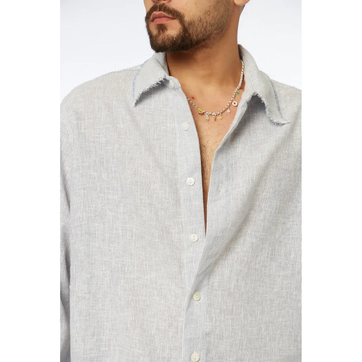 Close up of a man wearing a blue striped PURE long sleeve linen button-up shirt with a silver necklace with colorful charms