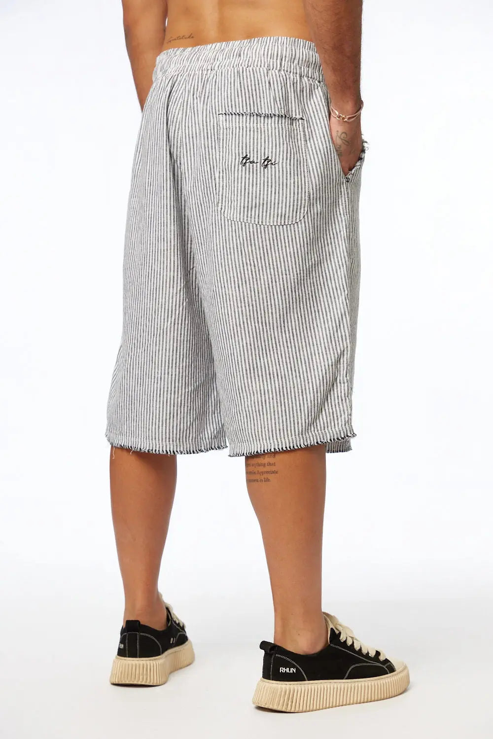 Rear view of a person wearing Striped Bermuda Shorts - Black, with a back pocket and raw hem