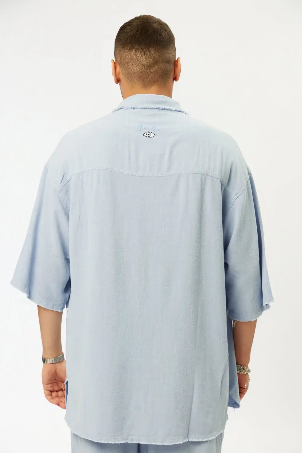 Man wearing a light blue shirt with a brand logo on the back against a white background