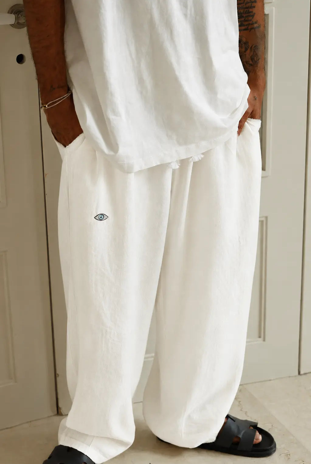 Pure Oversized Pants in cream white with an eye graphic, worn with a white t-shirt and black sandals