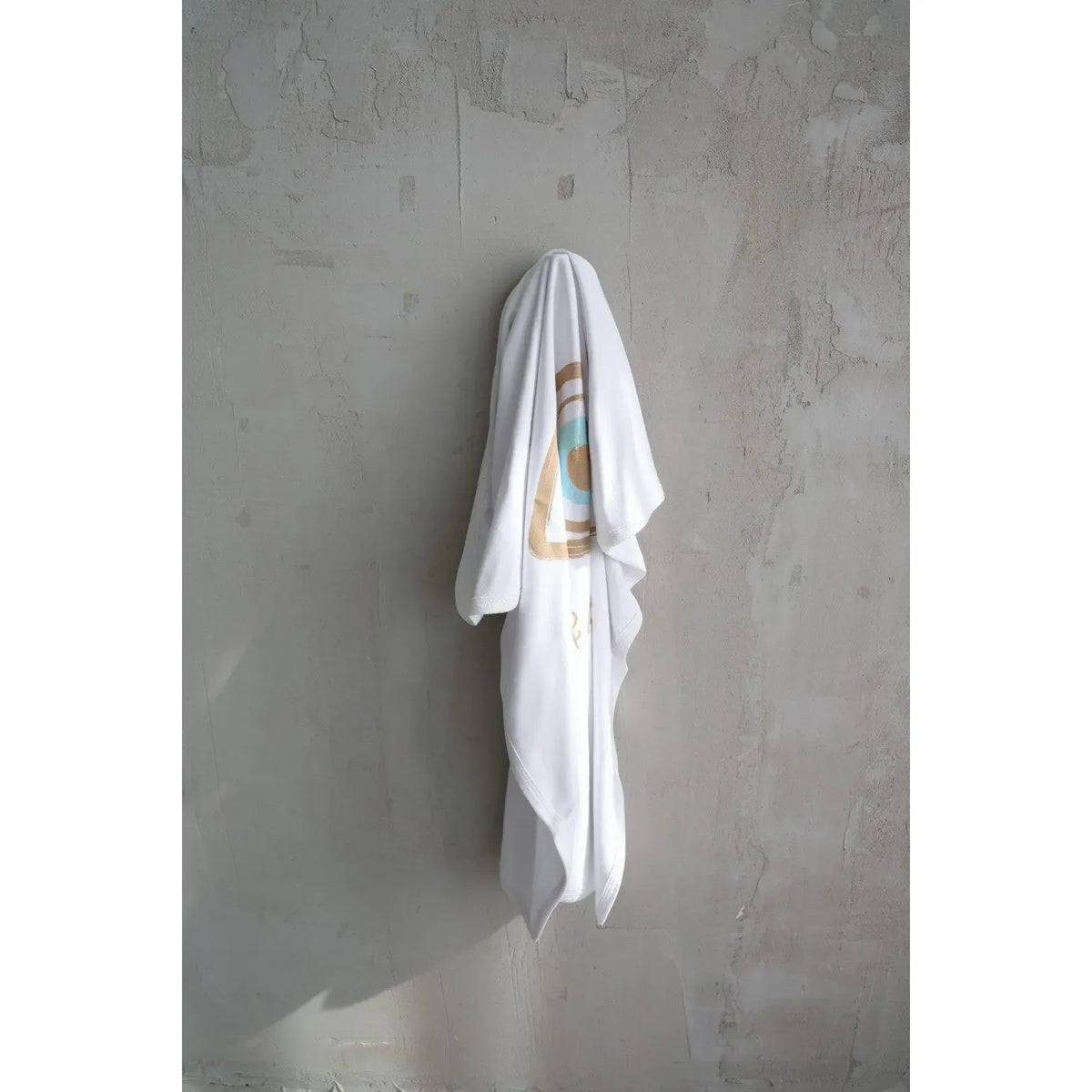 Cotton Single Elliptical Eye Blanket draped over a hook on a textured grey wall