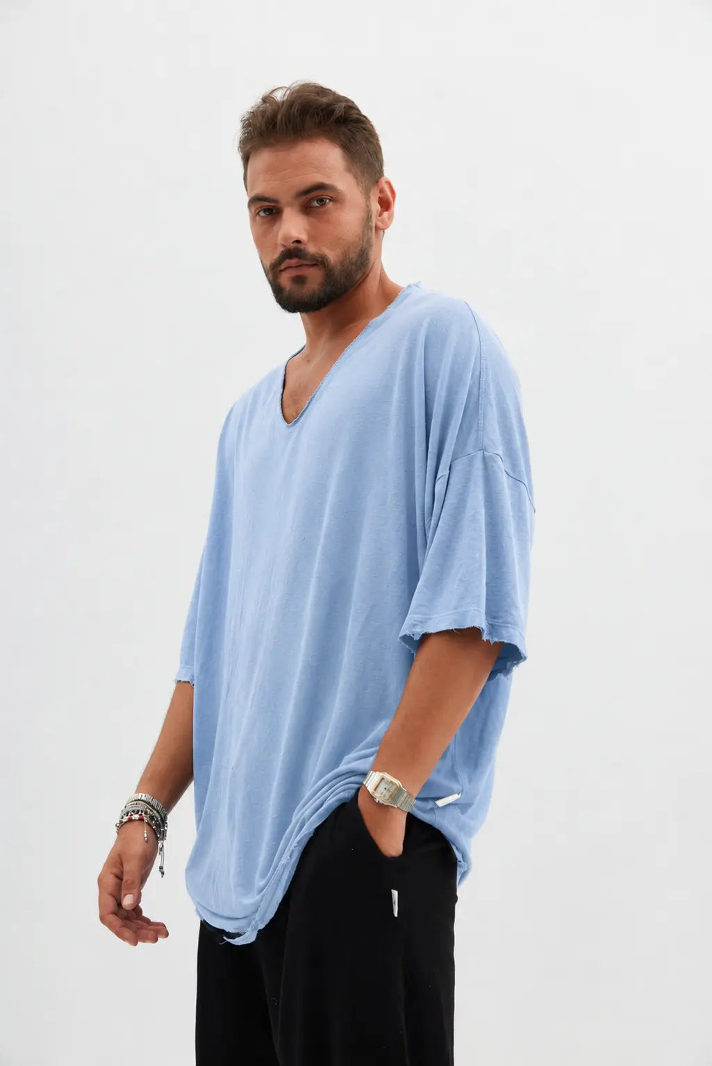 Man wearing a light blue Dor Oversized Shirt and black pants, with a watch and bracelets on his left wrist