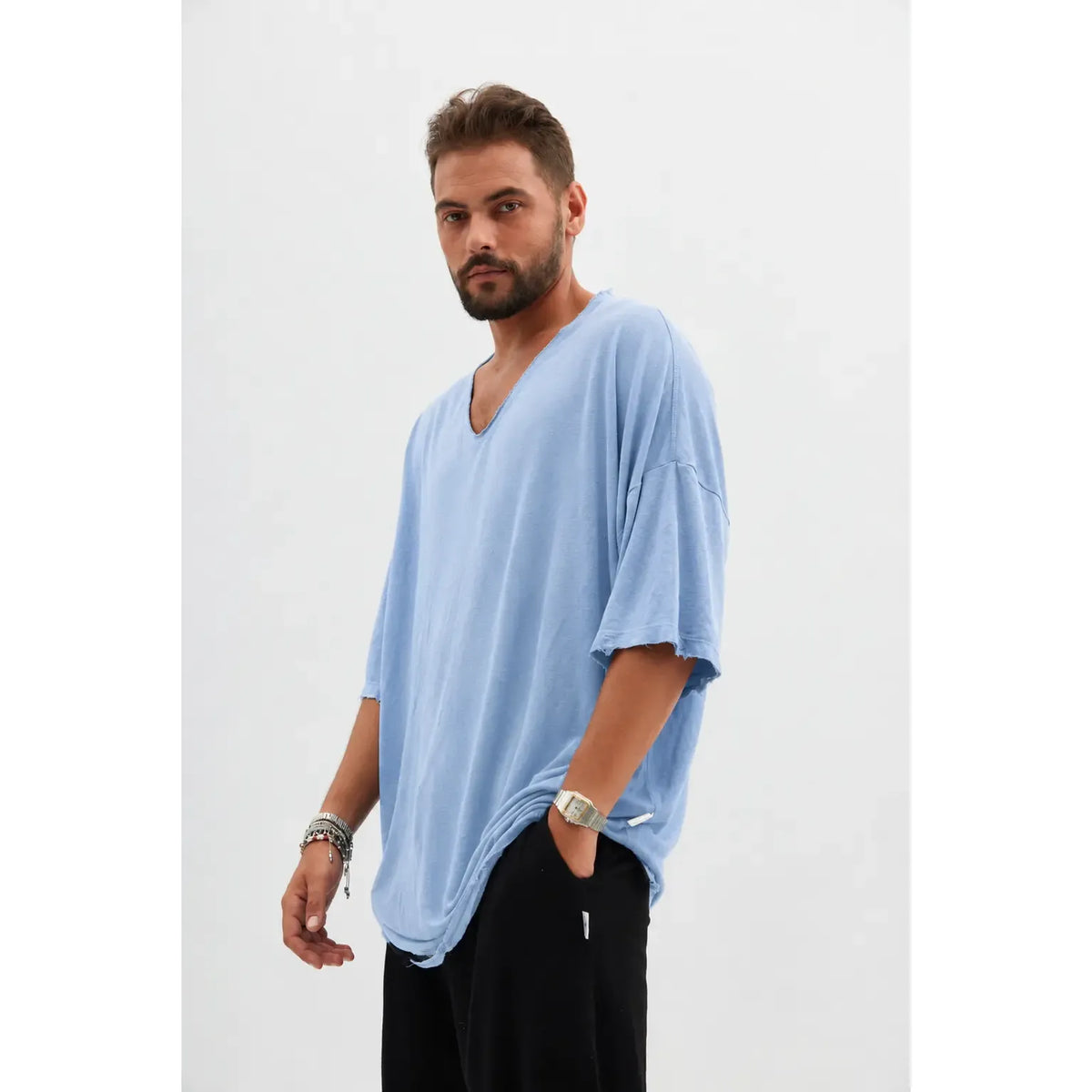 Man wearing a light blue Dor Oversized Shirt and black pants, with a watch and bracelets on his left wrist