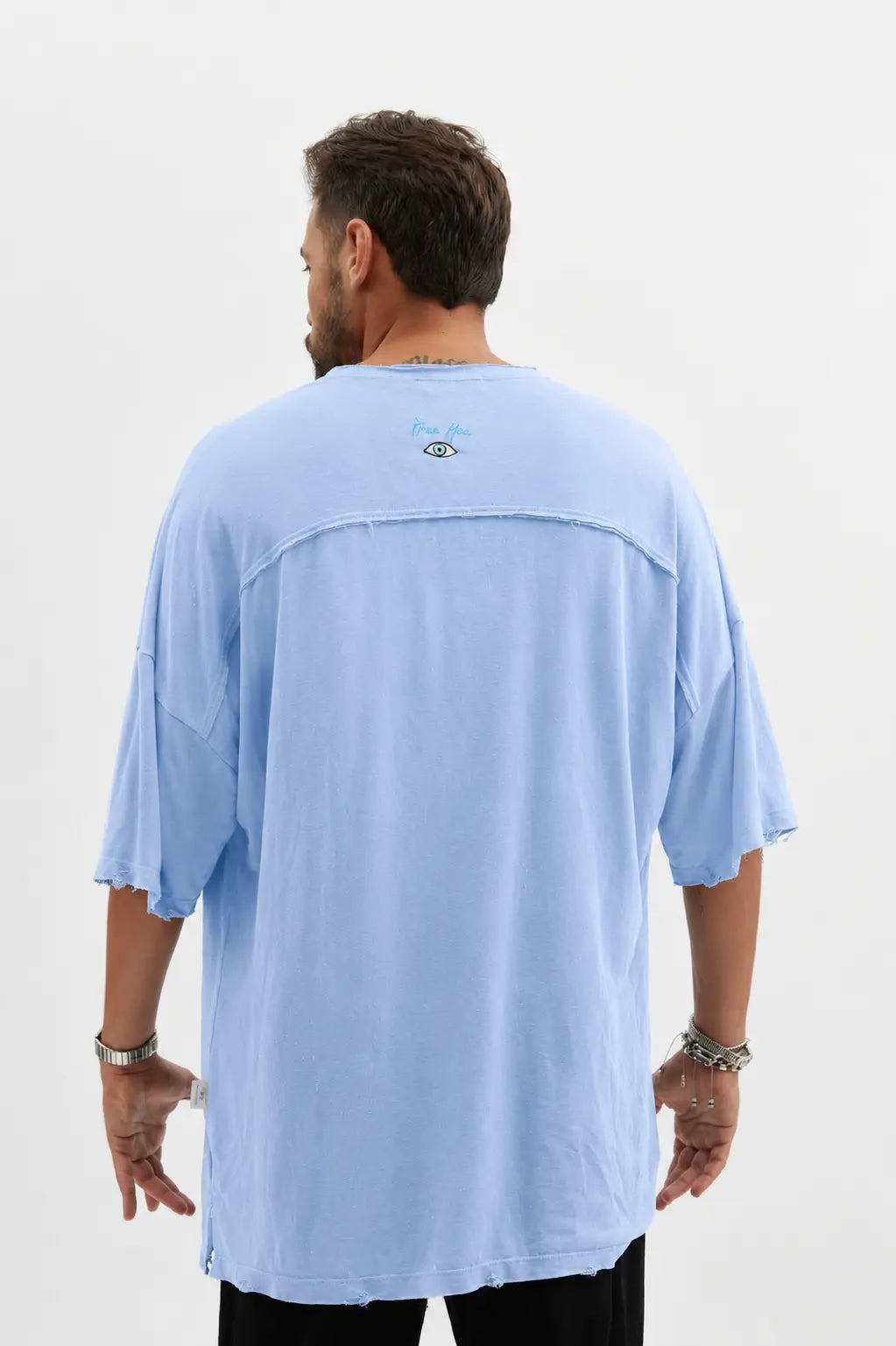 Back of a man wearing a light blue Dor Oversized Shirt with a small eye graphic and text on the upper back