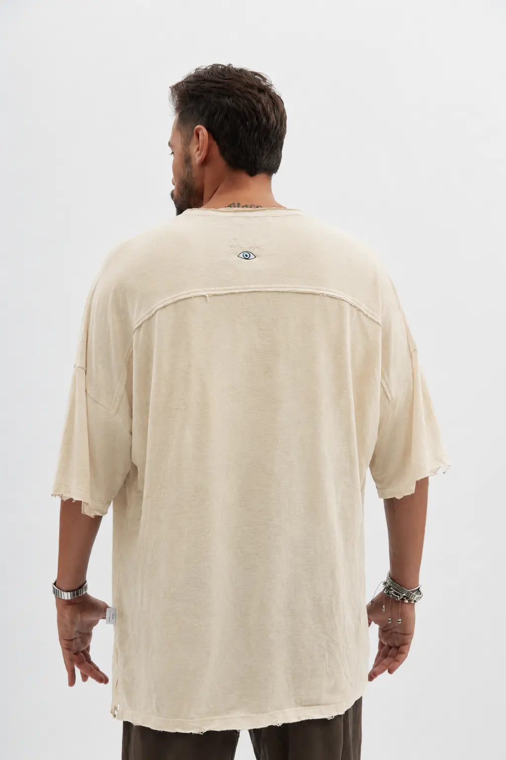 Back view of a man wearing a stone Dor Oversized Shirt with an eye graphic on the upper back
