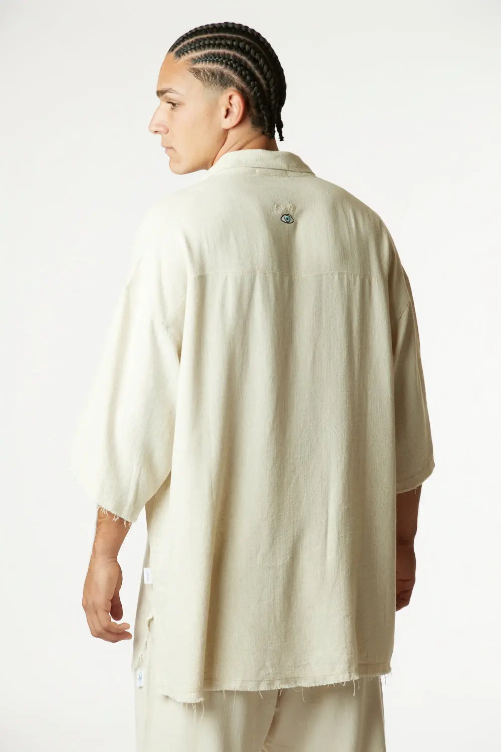 Man from behind wearing a Soft Linen Short Sleeve Button-Up Shirt in Melange Stone with an eye logo on the back