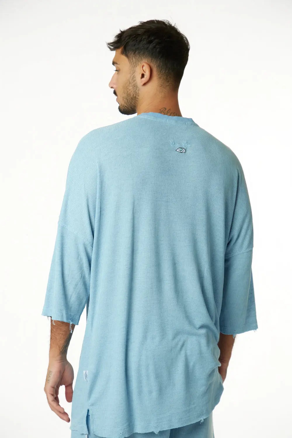 Man wearing a 3/4 Sleeve Nicki Rib in blue, seen from behind, with an eye graphic on the upper back
