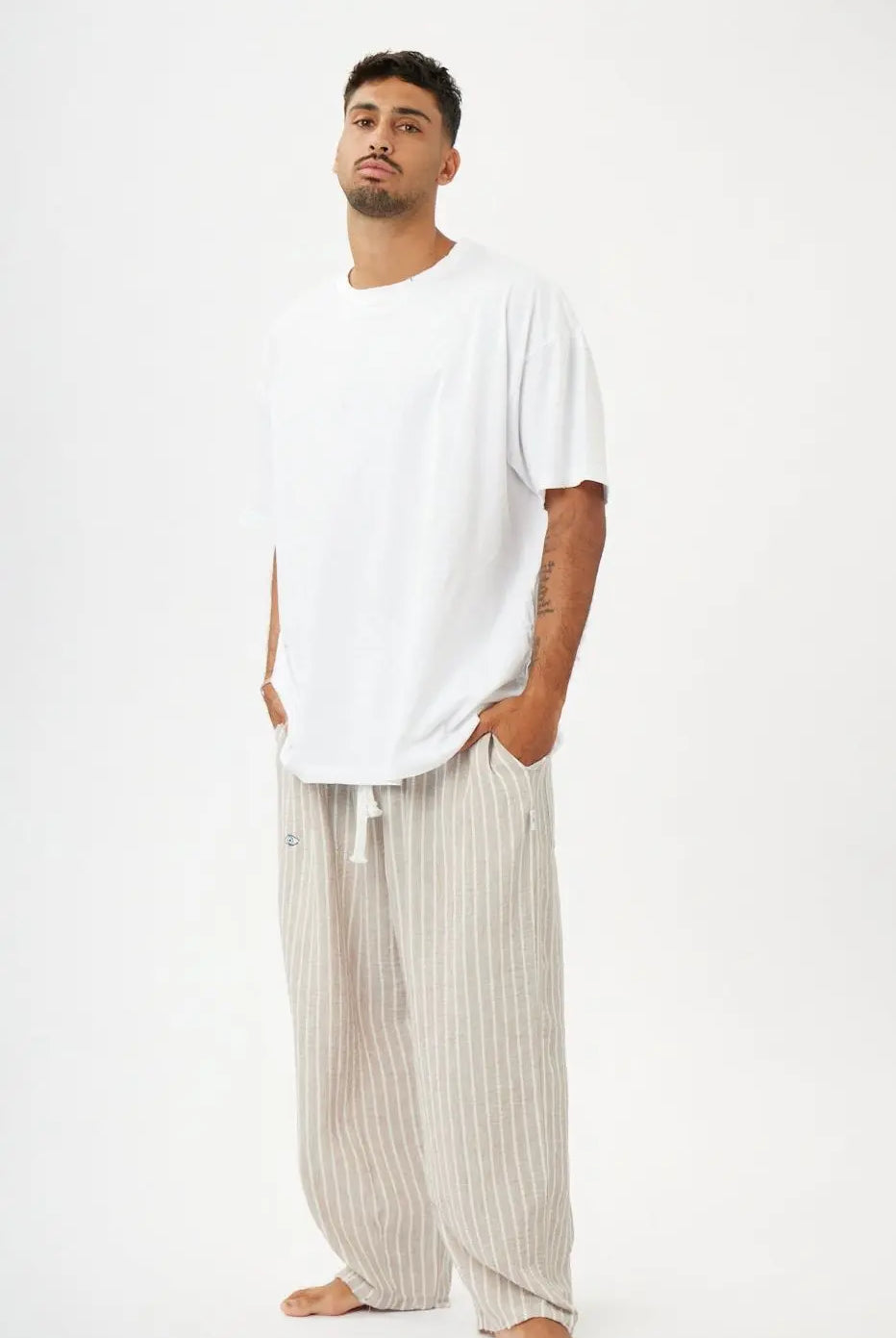 Man wearing a white oversized t-shirt and beige striped pants on a white background