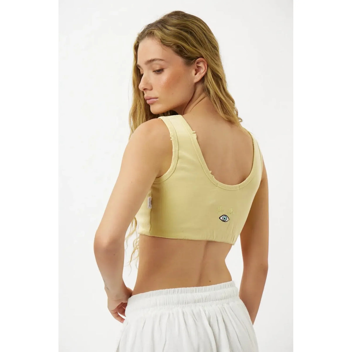 Back view of a woman wearing a yellow Essential Crop Top with an eye graphic on the back