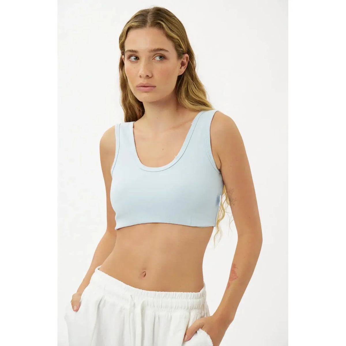Woman wearing a light blue sports bra and white pants on a plain background