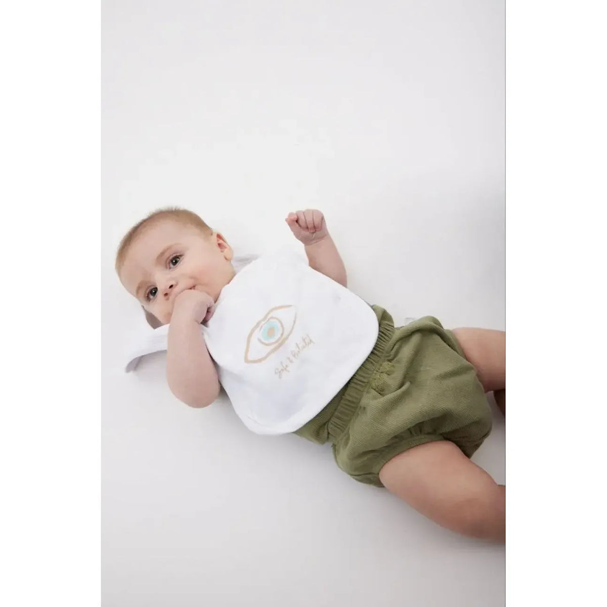 Newborn Cotton Bib with an eye graphic and Safe & Protected text, worn by a baby in green shorts