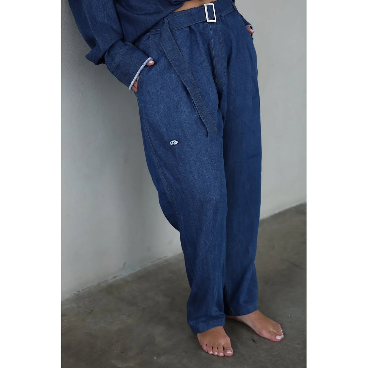 Dark Denim Pants with Belt, featuring a white eye logo on the left thigh and a silver rectangular belt buckle