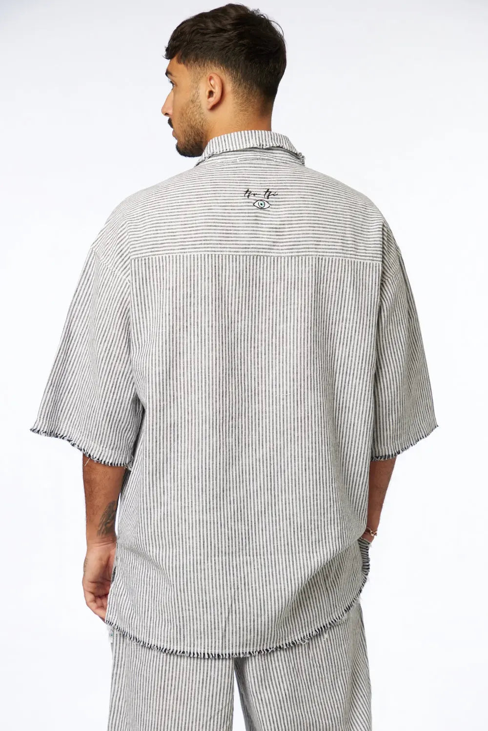 Man from behind wearing a black striped linen short sleeve button-up shirt with an eye graphic on the back