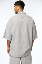 Man from behind wearing a black striped linen short sleeve button-up shirt with an eye graphic on the back