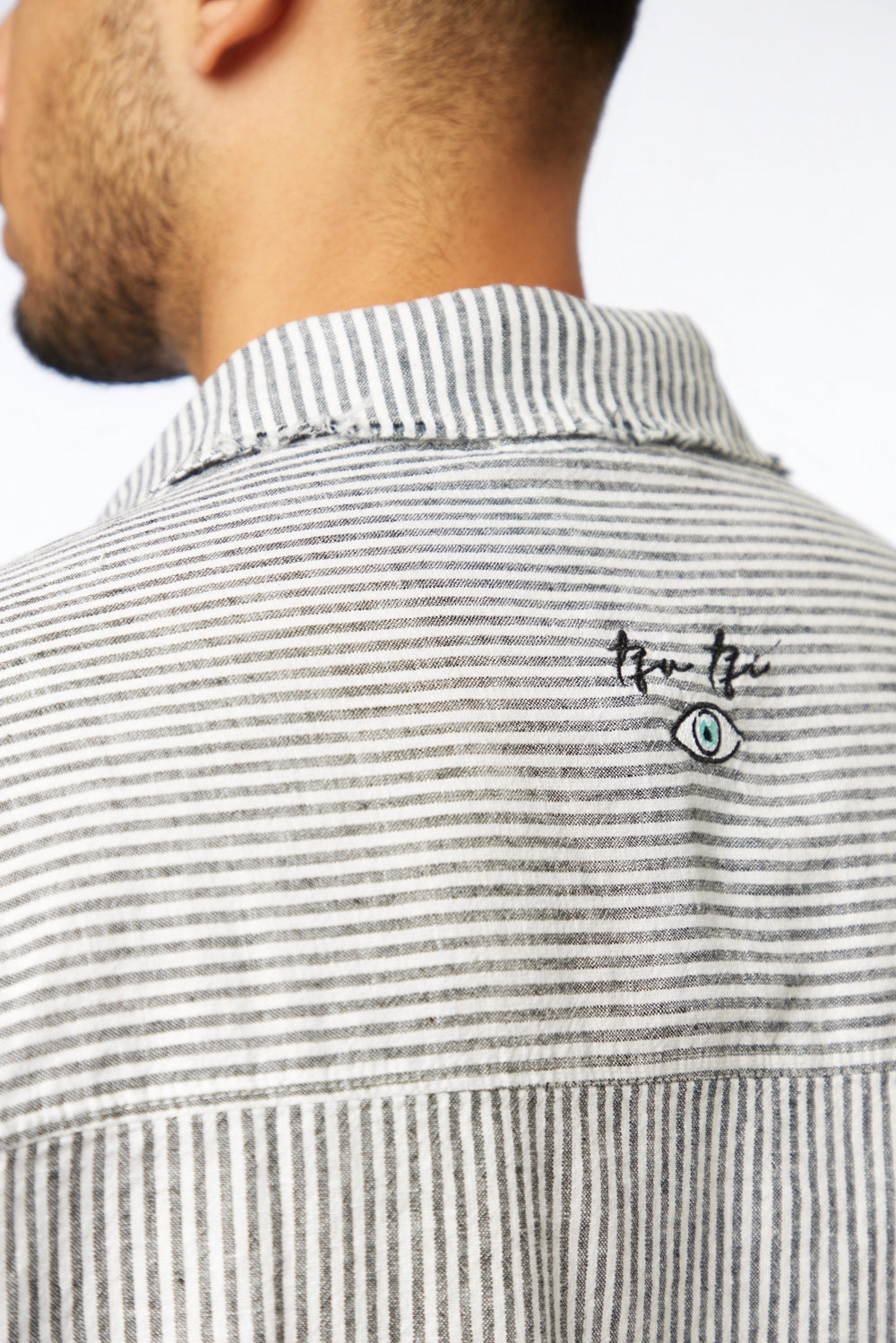 Close-up of a person wearing a striped shirt with a logo on the collar.