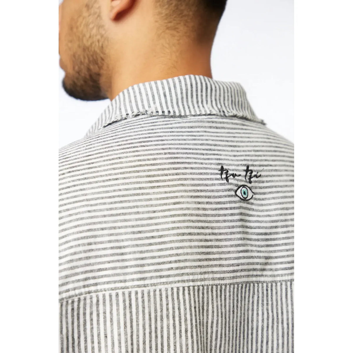 Close-up of a person wearing a striped shirt with a logo on the collar.