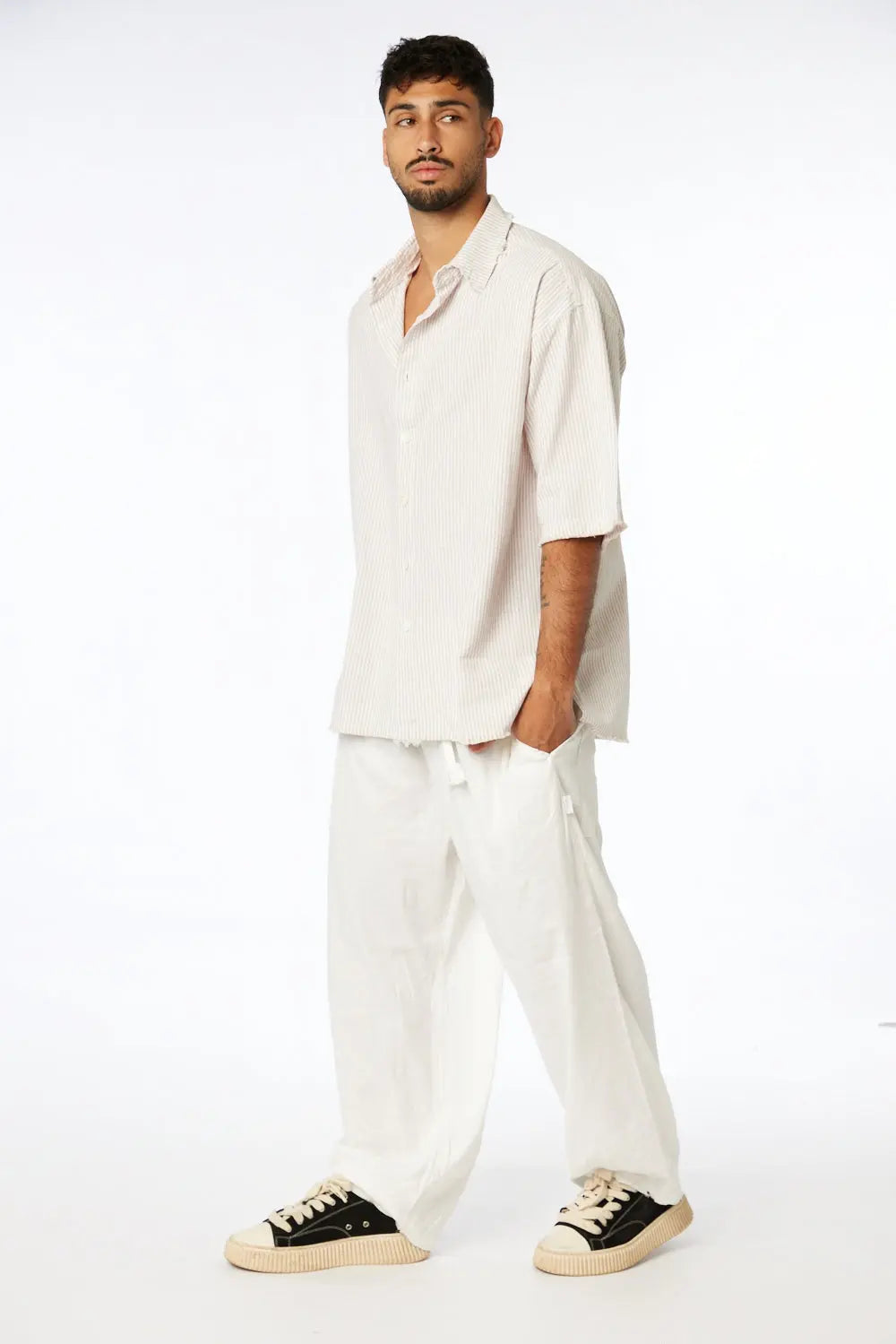 Man wearing a Striped Linen Short Sleeve Button-Up Shirt in Stone, white linen pants, and black and white sneakers