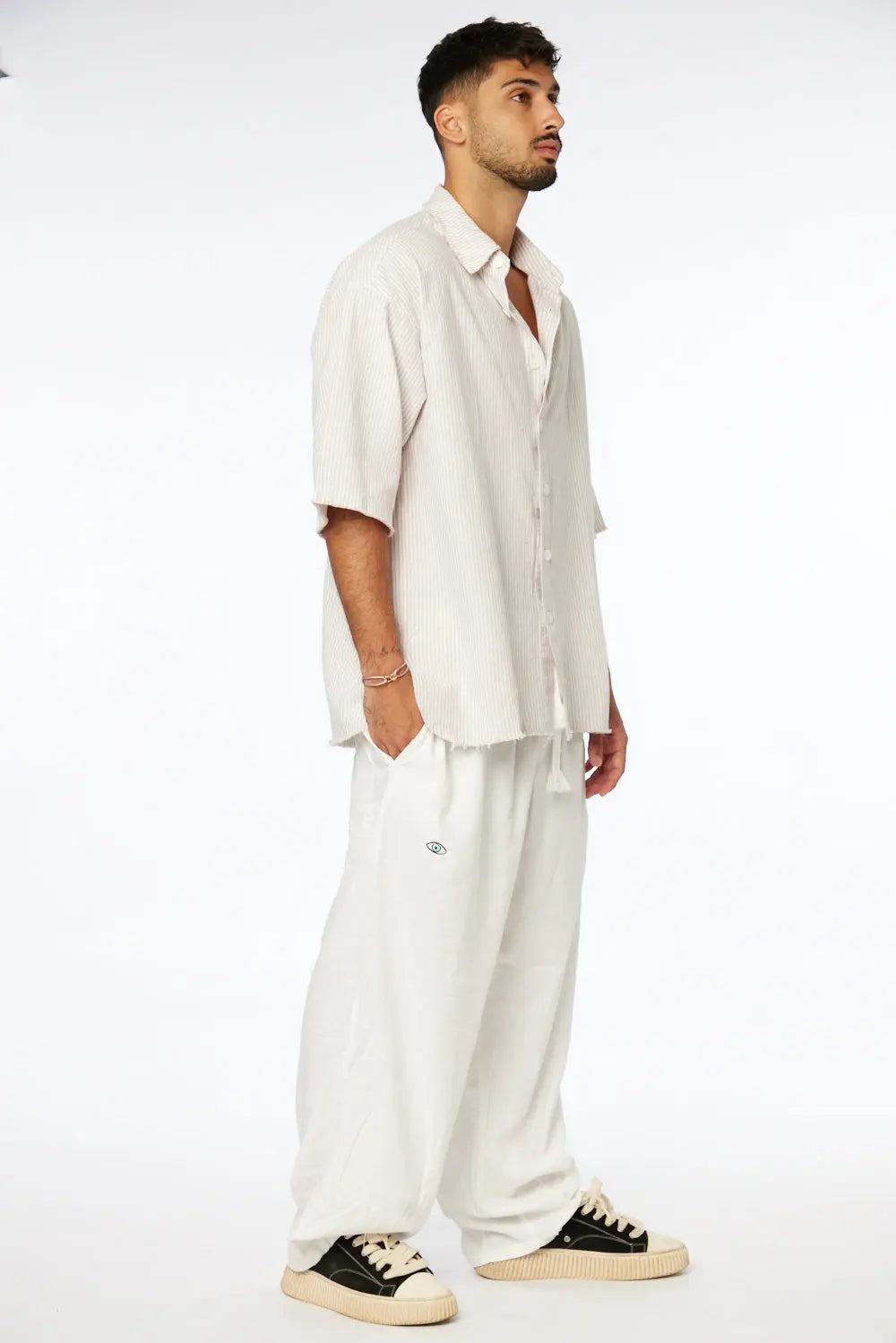 Man wearing a Striped Linen Short Sleeve Button-Up Shirt in Stone with white pants and black and white sneakers