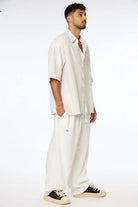 Man wearing a Striped Linen Short Sleeve Button-Up Shirt in Stone with white pants and black and white sneakers