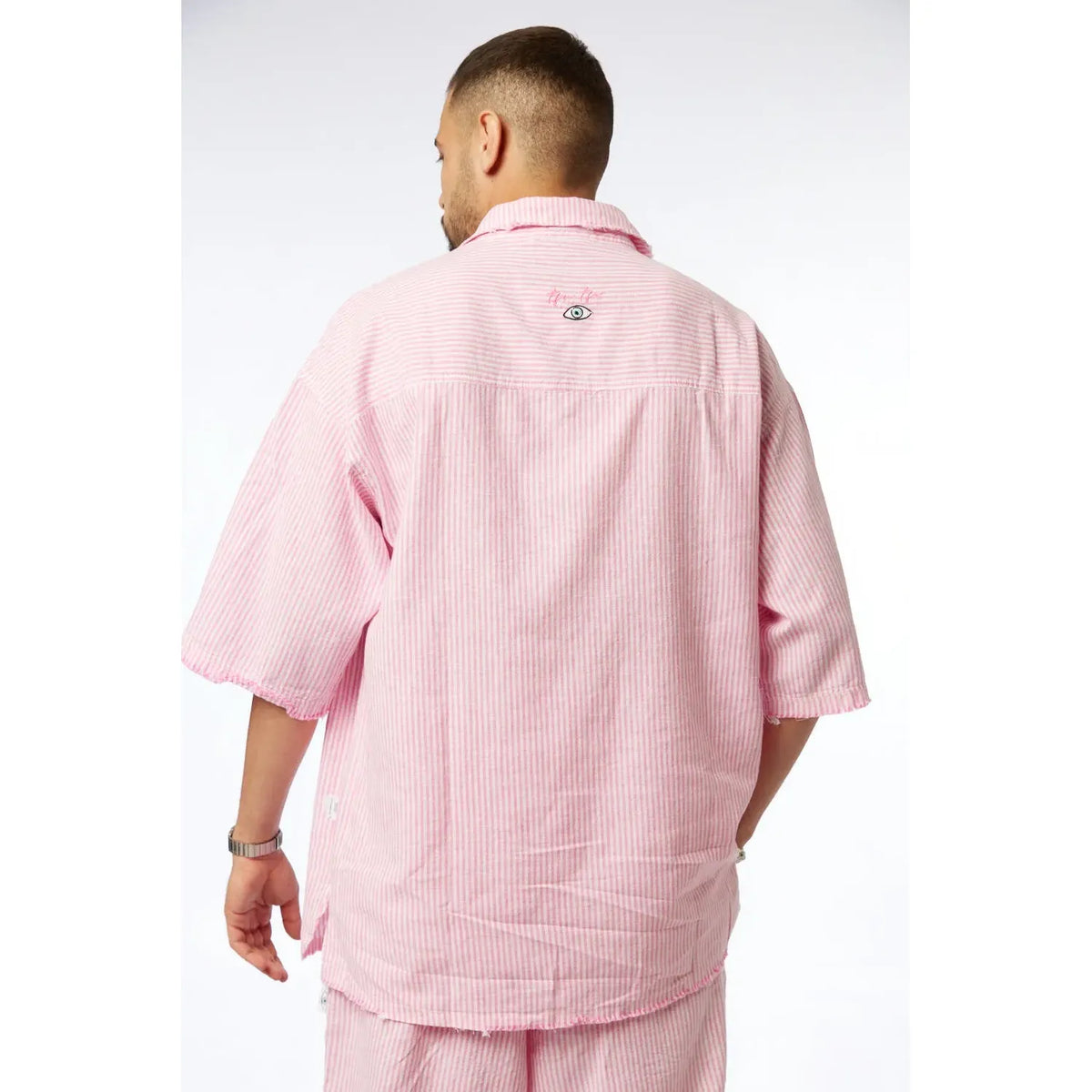 Back of a man wearing a pink striped linen short sleeve button-up shirt with an eye logo on the back