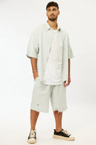 Man wearing a green striped linen short sleeve button-up shirt over a white t-shirt and matching striped shorts