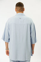Man wearing a light blue shirt with a brand logo on the back against a white background