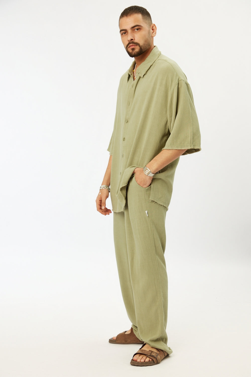 Man wearing a Soft Linen Short Sleeve Button-Up Shirt in green with matching green linen pants and brown sandals
