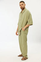 Man wearing a Soft Linen Short Sleeve Button-Up Shirt in green with matching green linen pants and brown sandals
