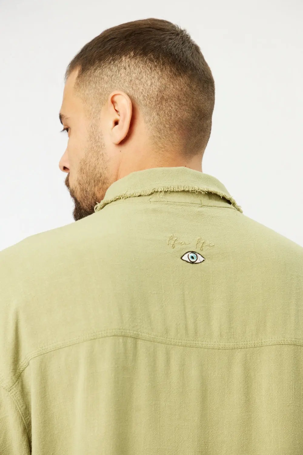 Back of a man wearing a green Soft Linen Short Sleeve Button-Up Shirt with an embroidered eye design