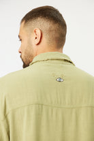 Back of a man wearing a green Soft Linen Short Sleeve Button-Up Shirt with an embroidered eye design
