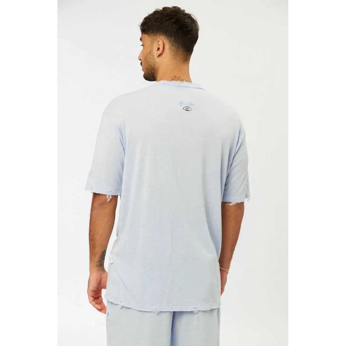 Back of Nicki Soft Open Top in light blue, with distressed details on sleeves and hem, and a small eye graphic on the upper back
