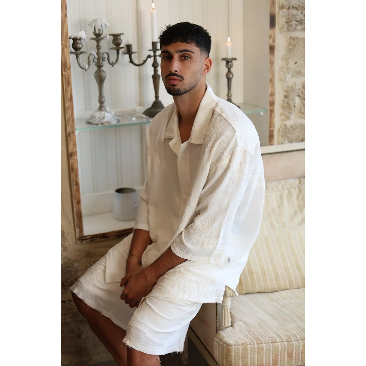 Man wearing a white SPARKS 3/4 Sleeve Button-Up Shirt, sitting on a couch with candelabras in the background
