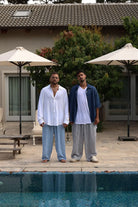 Two men in Pure Oversized Linen Pants, one in blue and white stripes, the other in grey and white stripes, by a pool