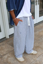 Pure Oversized Linen Pants in blue and white stripes, worn with a white t-shirt, blue denim shirt, and espadrilles