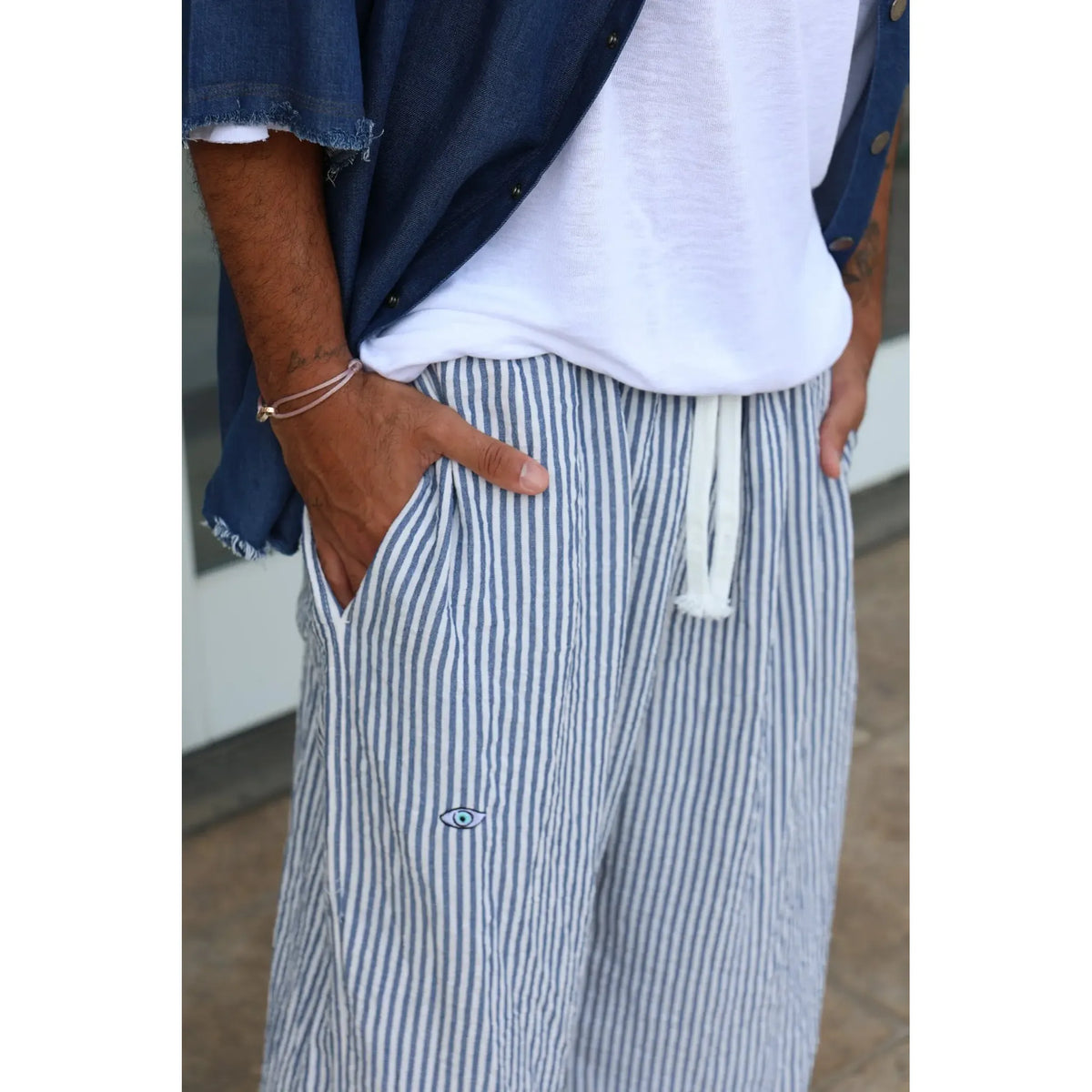 Pure Oversized Linen Pants in blue and white stripes with a white drawstring and an evil eye emblem