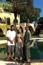 Three people in matching zebra print outfits standing by a pool with palm trees and a building in the background.