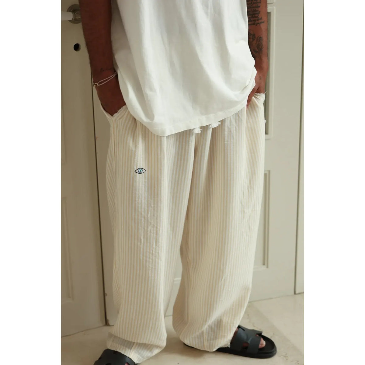 Pure Oversized Linen Pants in yellow and white stripes with an eye graphic, worn by a person in black sandals