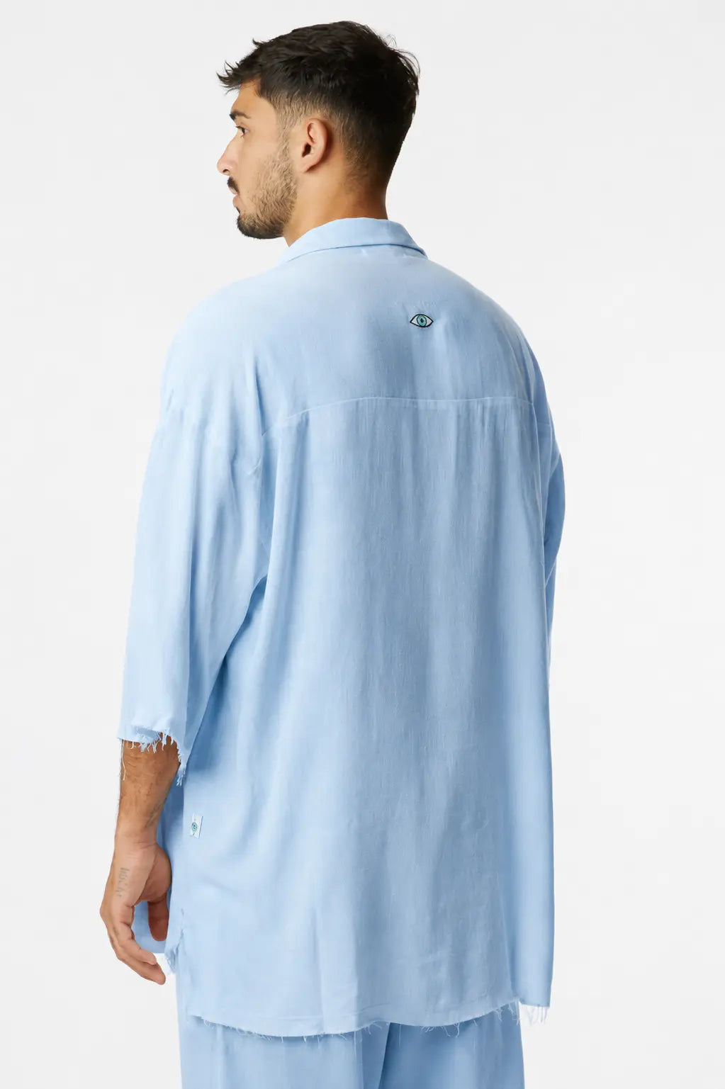 Man from behind wearing a light blue Soft Linen Short Sleeve Button-Up Shirt with an eye logo on the back