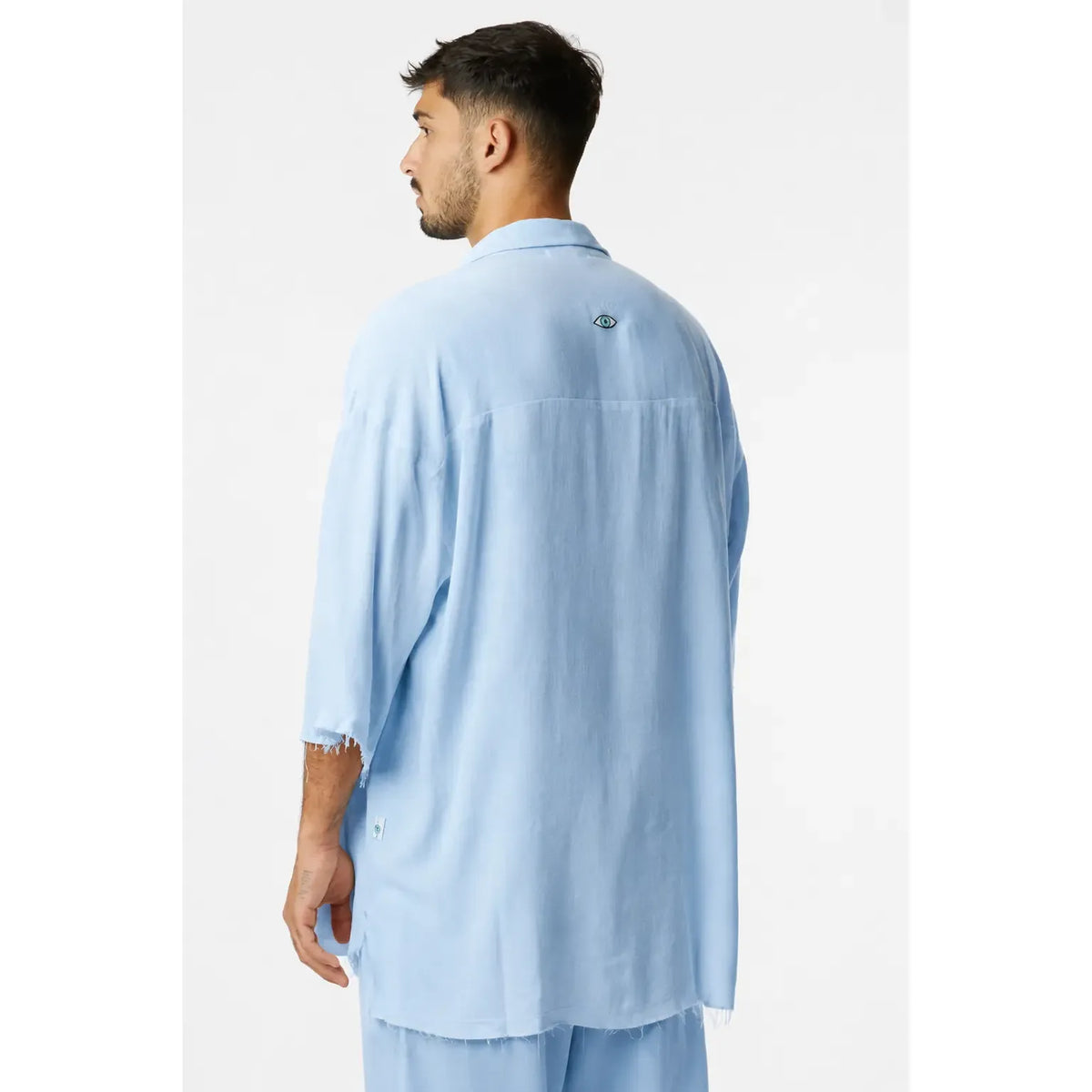 Man from behind wearing a light blue Soft Linen Short Sleeve Button-Up Shirt with an eye logo on the back