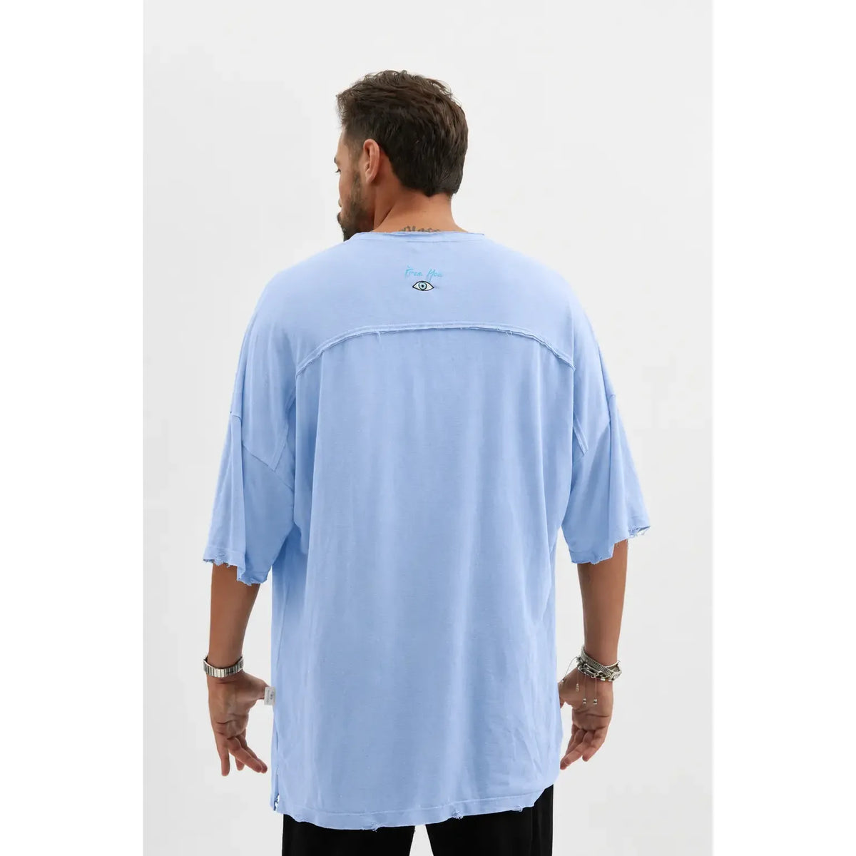 Back of a man wearing a light blue Dor Oversized Shirt with a small eye graphic and text on the upper back