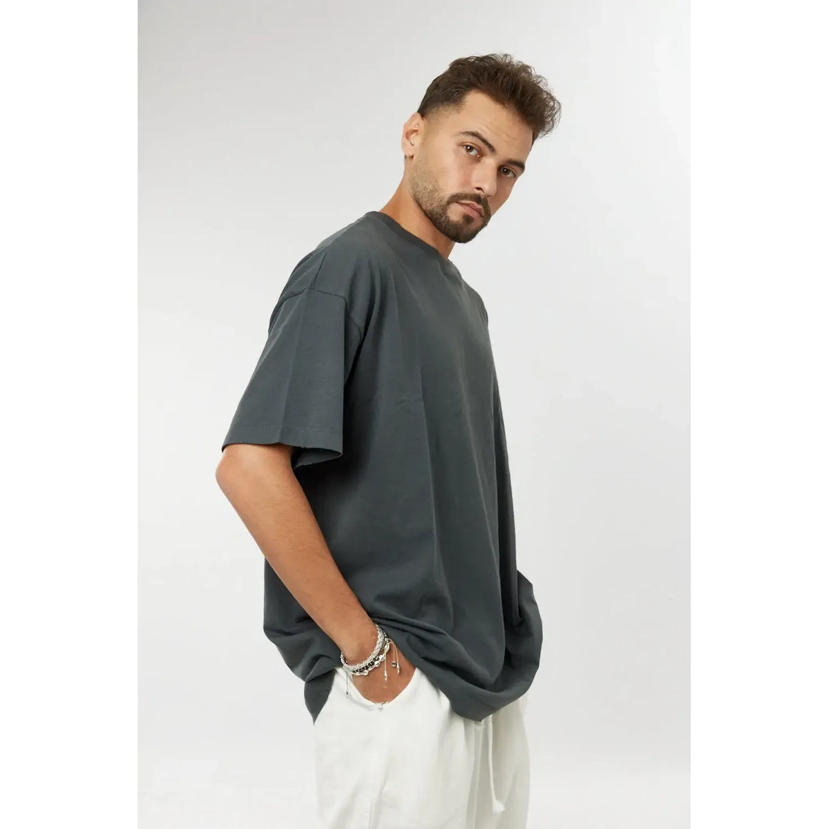 Man wearing a grey cotton t-shirt and white trousers, with a hand in his pocket