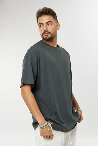 Man wearing a grey cotton t-shirt and white trousers, looking over his right shoulder
