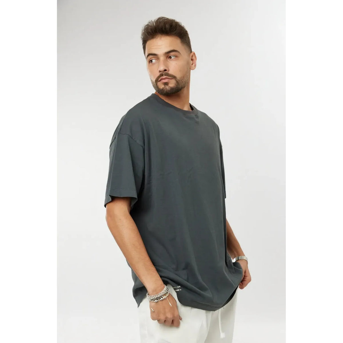 Man wearing a grey cotton t-shirt and white trousers, looking over his right shoulder