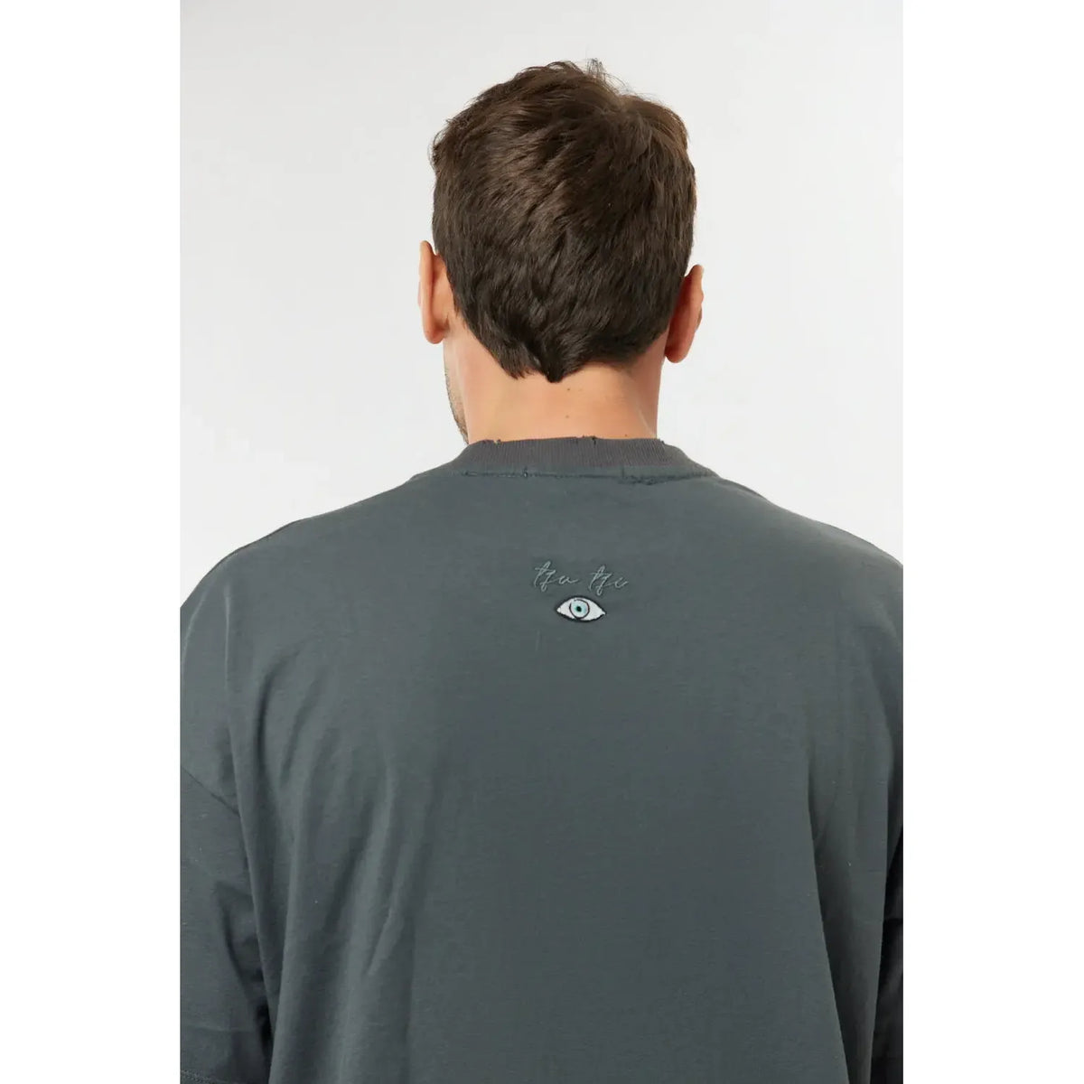 Back of a man wearing a grey Cotton T-Shirt with a small eye graphic and text below the collar