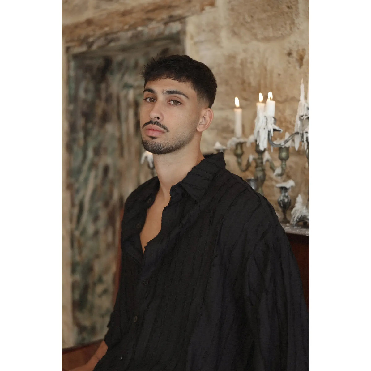 Man wearing a black RIPS Short Sleeve Button-Up Shirt with textured fabric, standing in front of a stone wall with lit candles