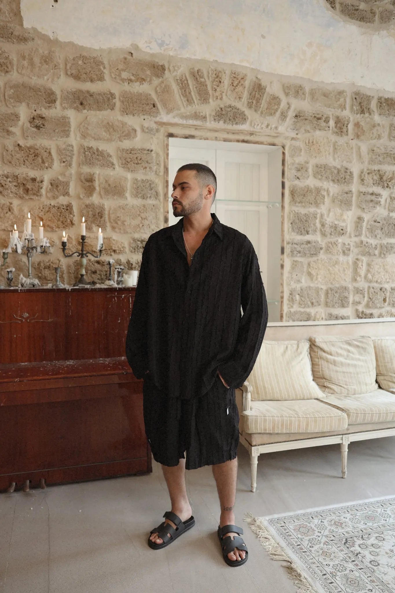 Man wearing black RIPS LONG SLEEVE SET with sandals in a room with stone walls and antique furniture