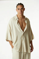 Soft Linen Short Sleeve Button-Up Shirt in Melange Stone, worn by a man with braided hair, standing with one hand in his pocket