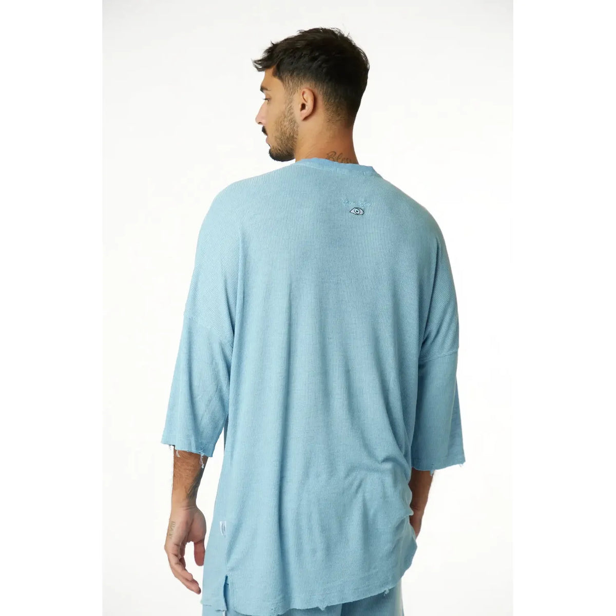 Man wearing a 3/4 Sleeve Nicki Rib in blue, seen from behind, with an eye graphic on the upper back