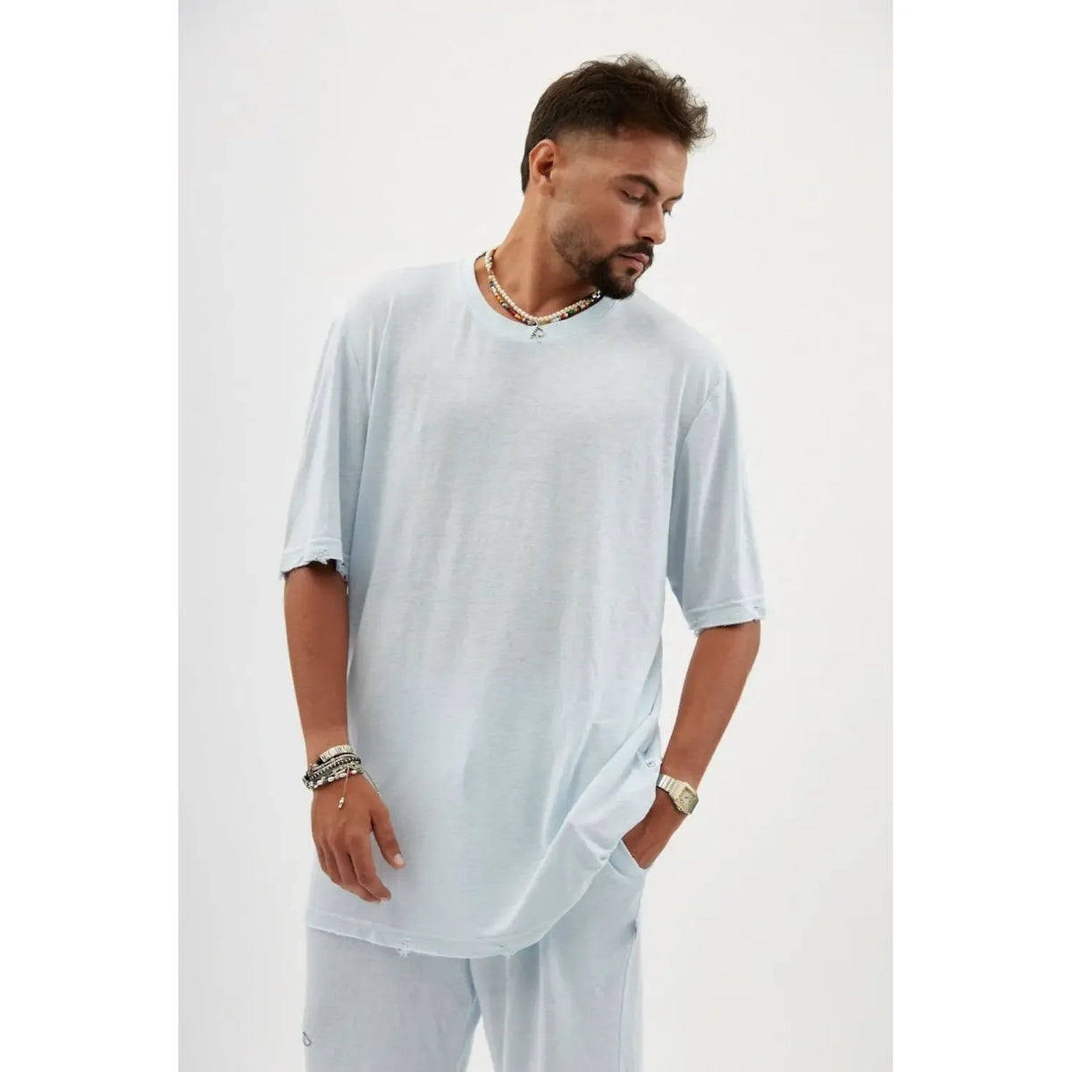 Man wearing a TFU Soft Essential Tee in sky blue with a beaded necklace and bracelets