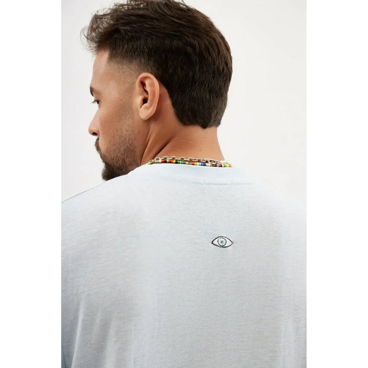 Back of a man wearing a sky blue TFU Soft Essential Tee with a small eye graphic and TFU logo embroidered on the upper back